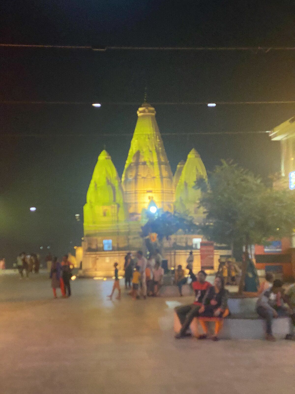 The temple's three spires lit in gold at night, with visitors in the courtyard