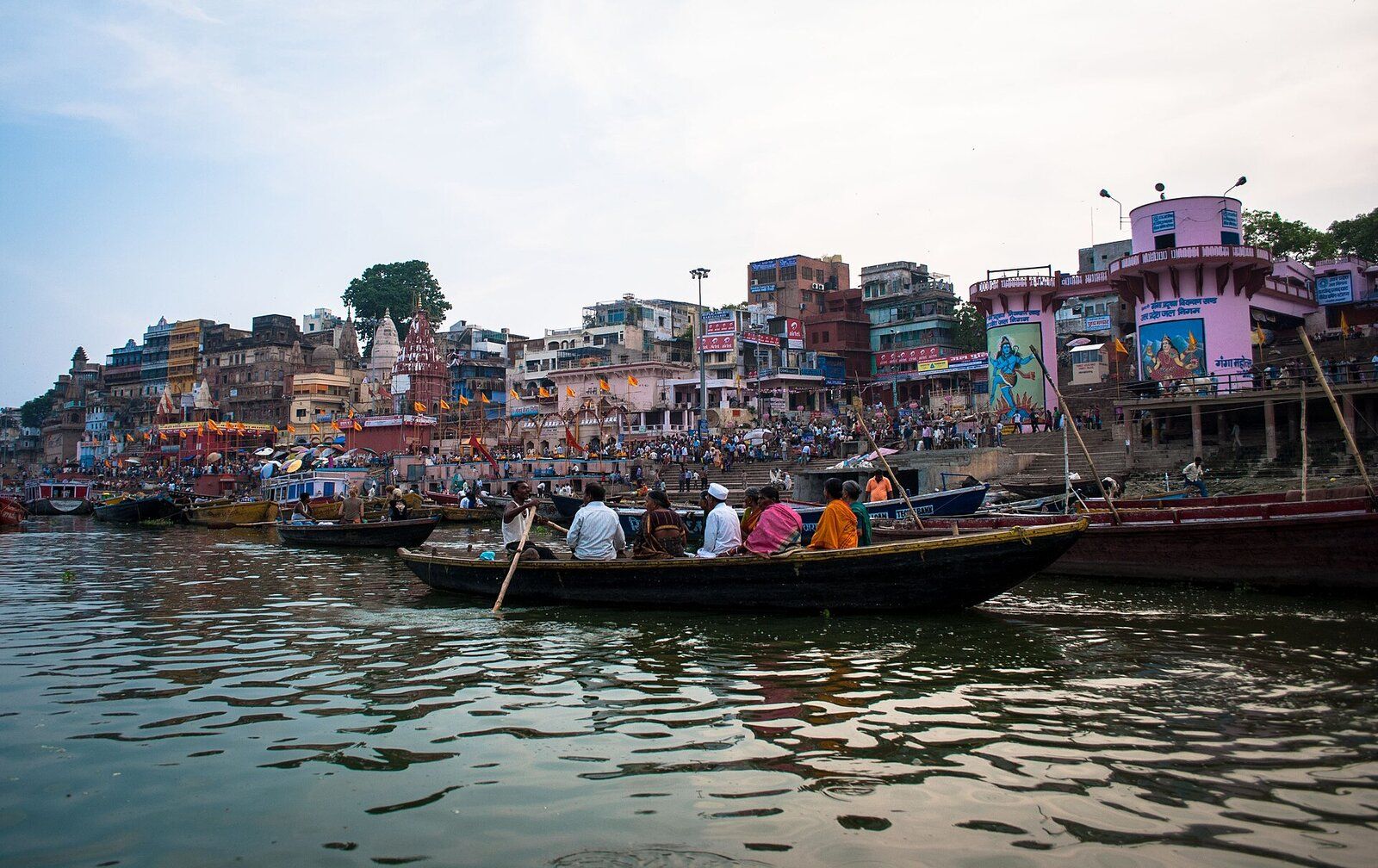Rows of wooden boats on the Ganga in front of the crowded ghat steps and old buildings